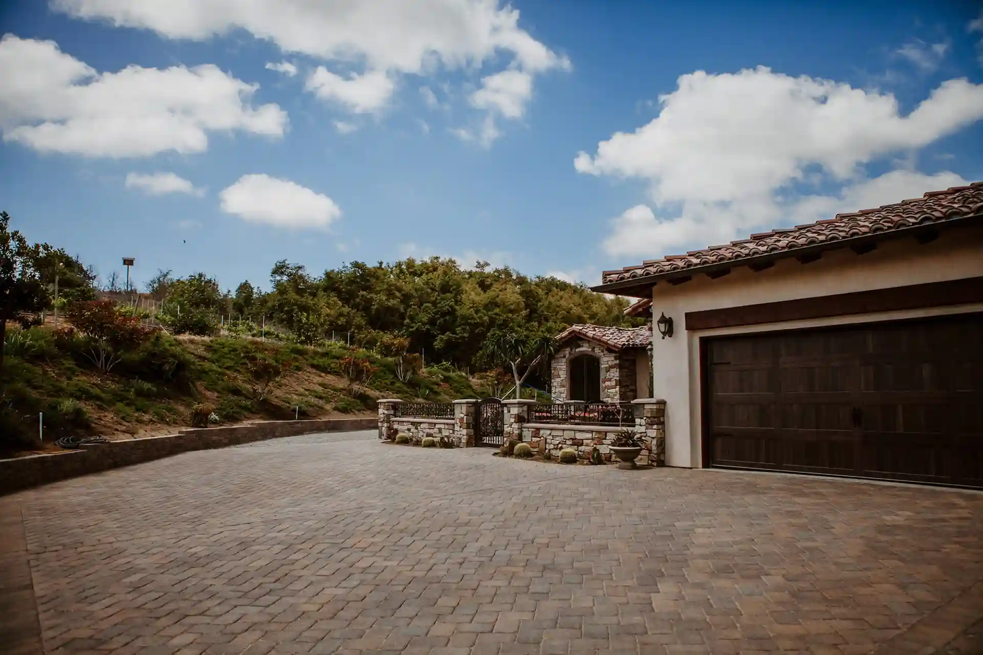 Photo of spacious stone-paved driveway leading to rustic stone-accented home.
